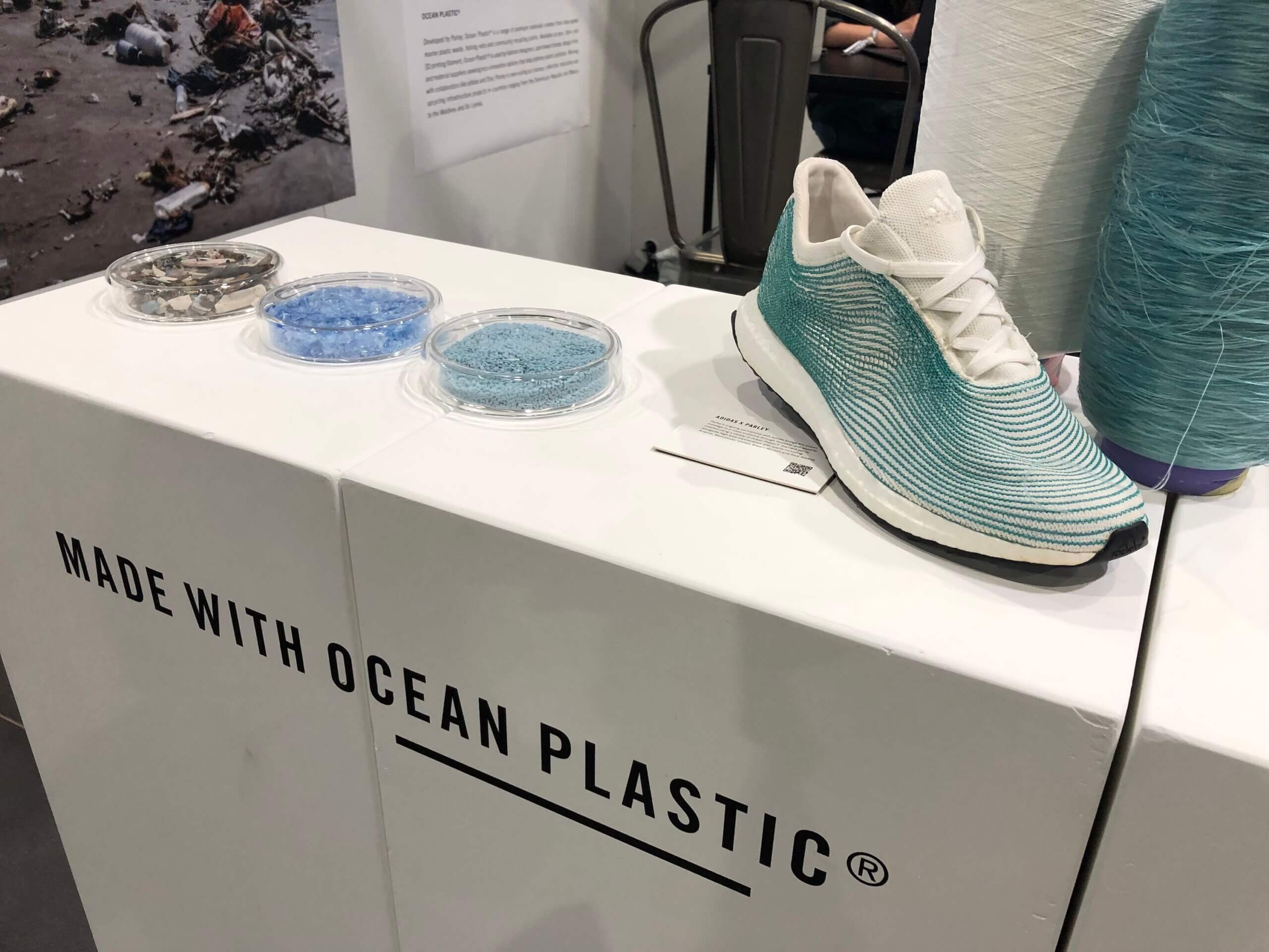 Store display with a blue green trainer and some micro plastics in dishes. The sign on the display says "Made with ocean plastics"