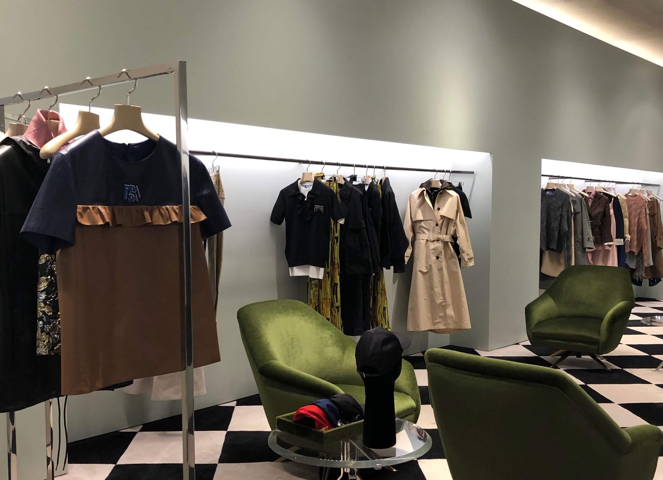 clothes hanging on rails in a showroom with green arm chairs